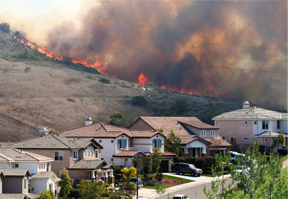 Wildfire approaching homes on a hillside, the scenario insurance inspectors assess properties against